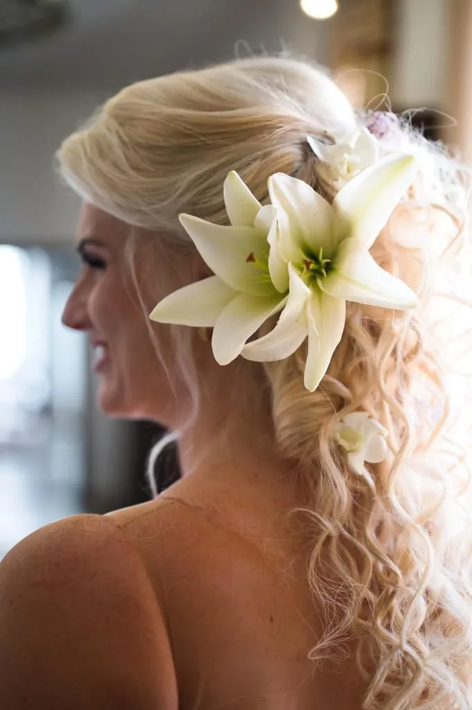 Blonde Braut von der Seite mit langen Locken und großen weißen Lilien im Haar